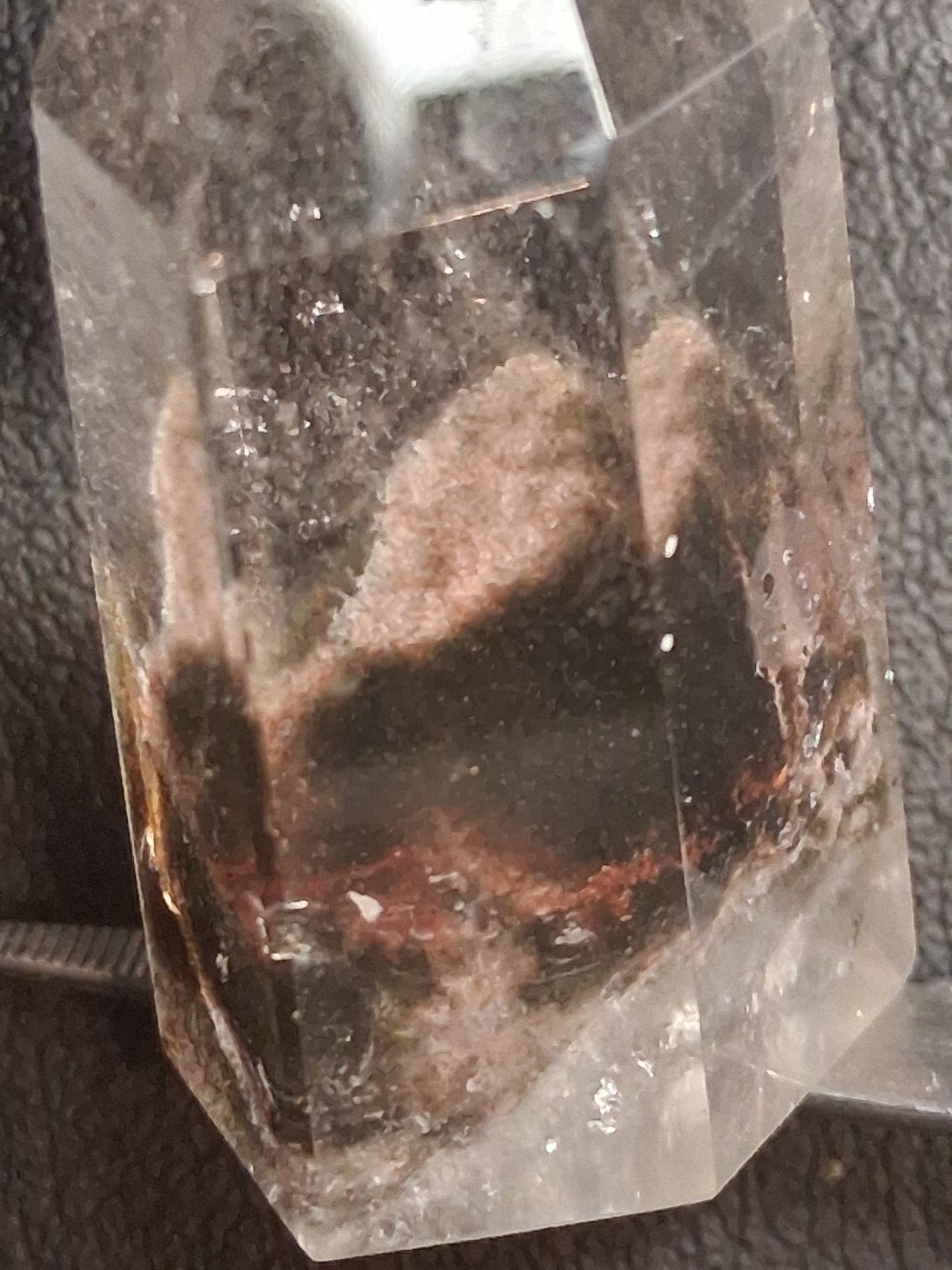 A clear quartz crystal point featuring prominent brown and black inclusions, photographed close-up against a dark textured background.