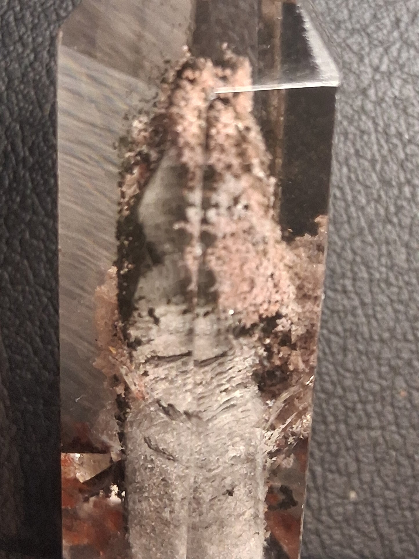 A clear quartz crystal point showing natural inclusions and a textured gray and brown matrix, photographed close-up on a black textured surface.